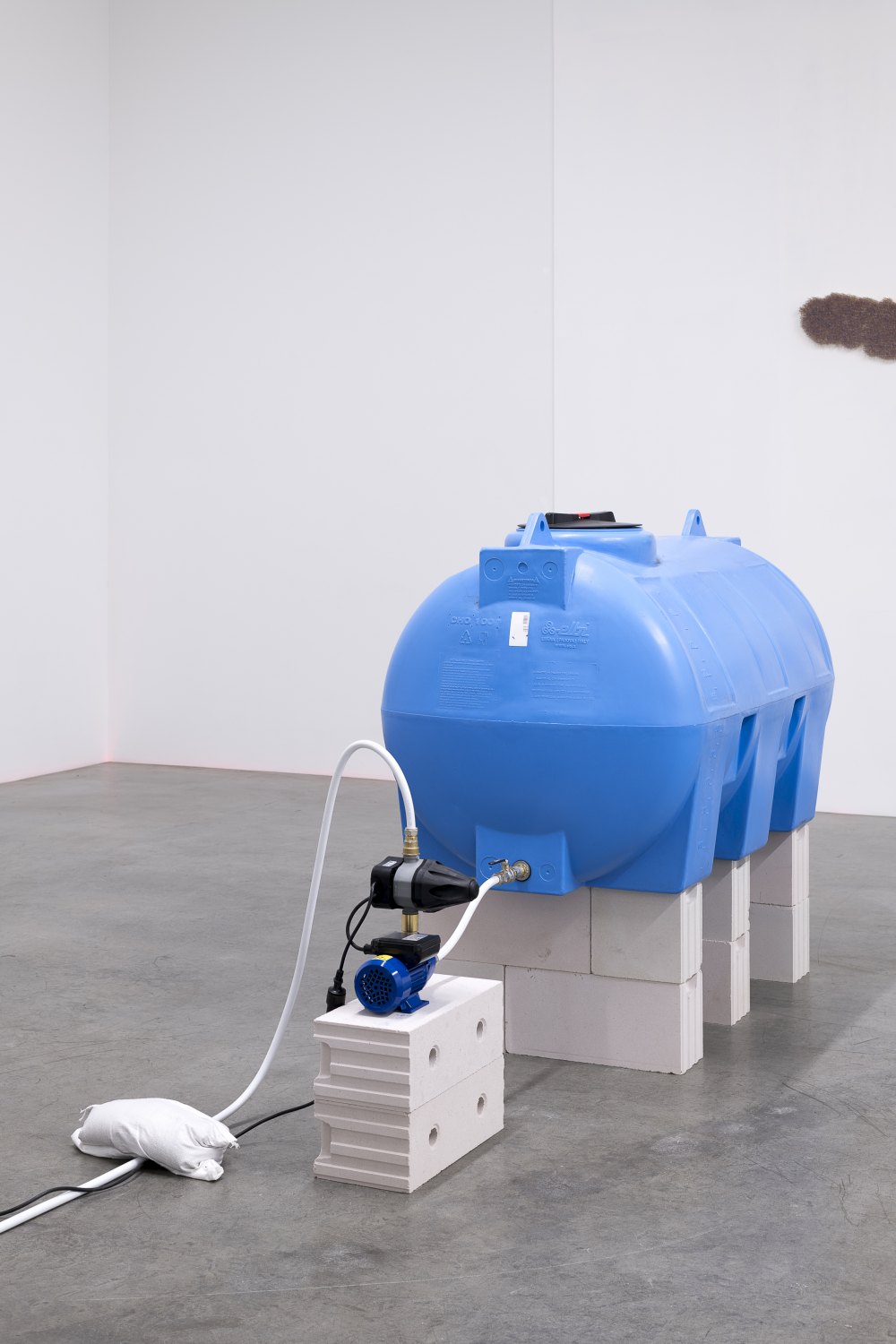 Claire Fontaine La mer à Boire, 2023 1000L blue water tank, pump, automatic pressure controller, 20 mm flexible hydraulic pipe, wall mounted drinking fountain, 80 mm drainage pipes, gerry can, cables, wall mountings and breeze blocks, mains water with 38 grams of salt per litre dimensions variable
